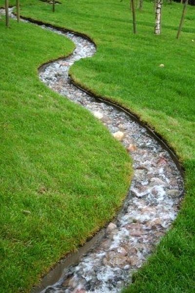 A running stream water feature made with curved corten steel channels and finished with a pebble bed